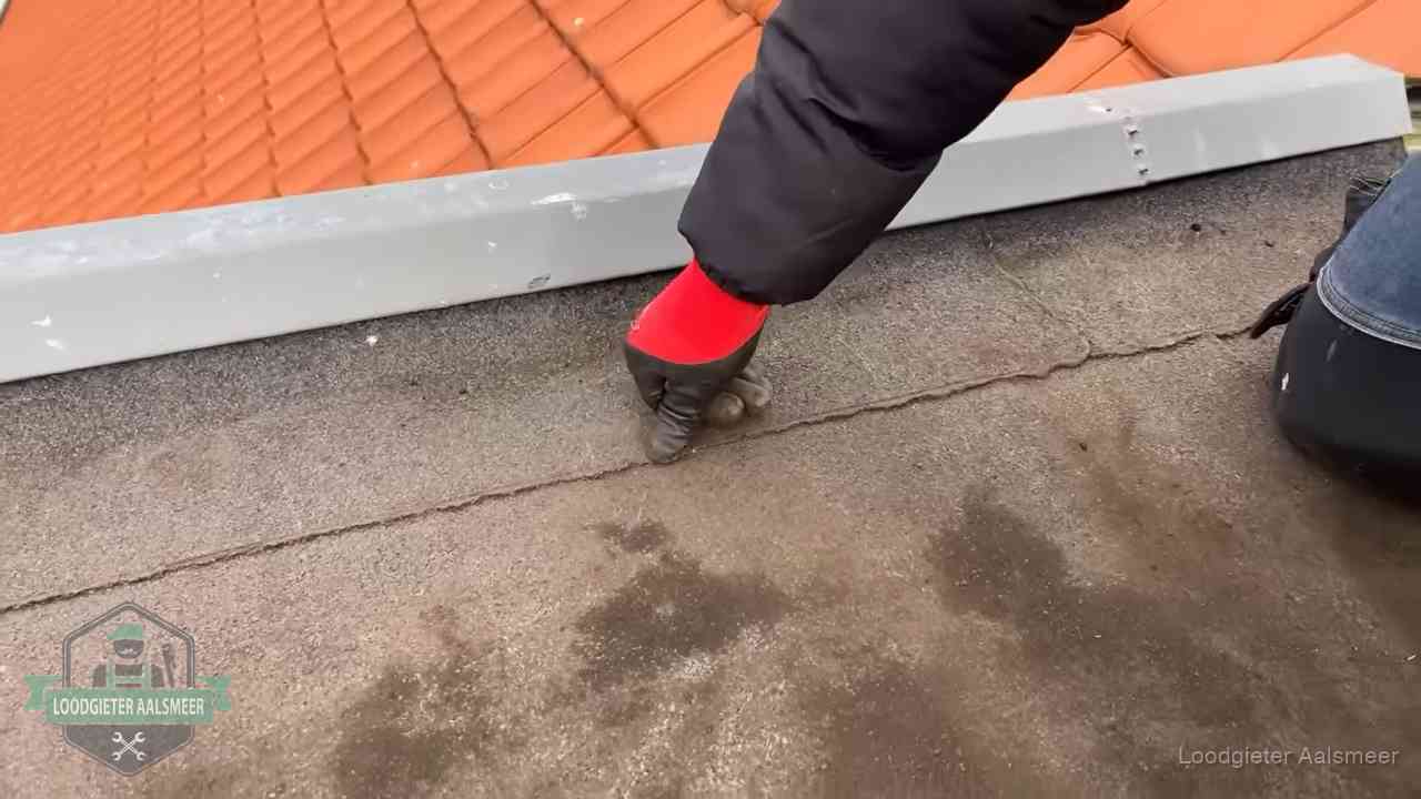 Vakman wijst een naad met vochtplekken aan op een bitumen plat dak in Aalsmeer
