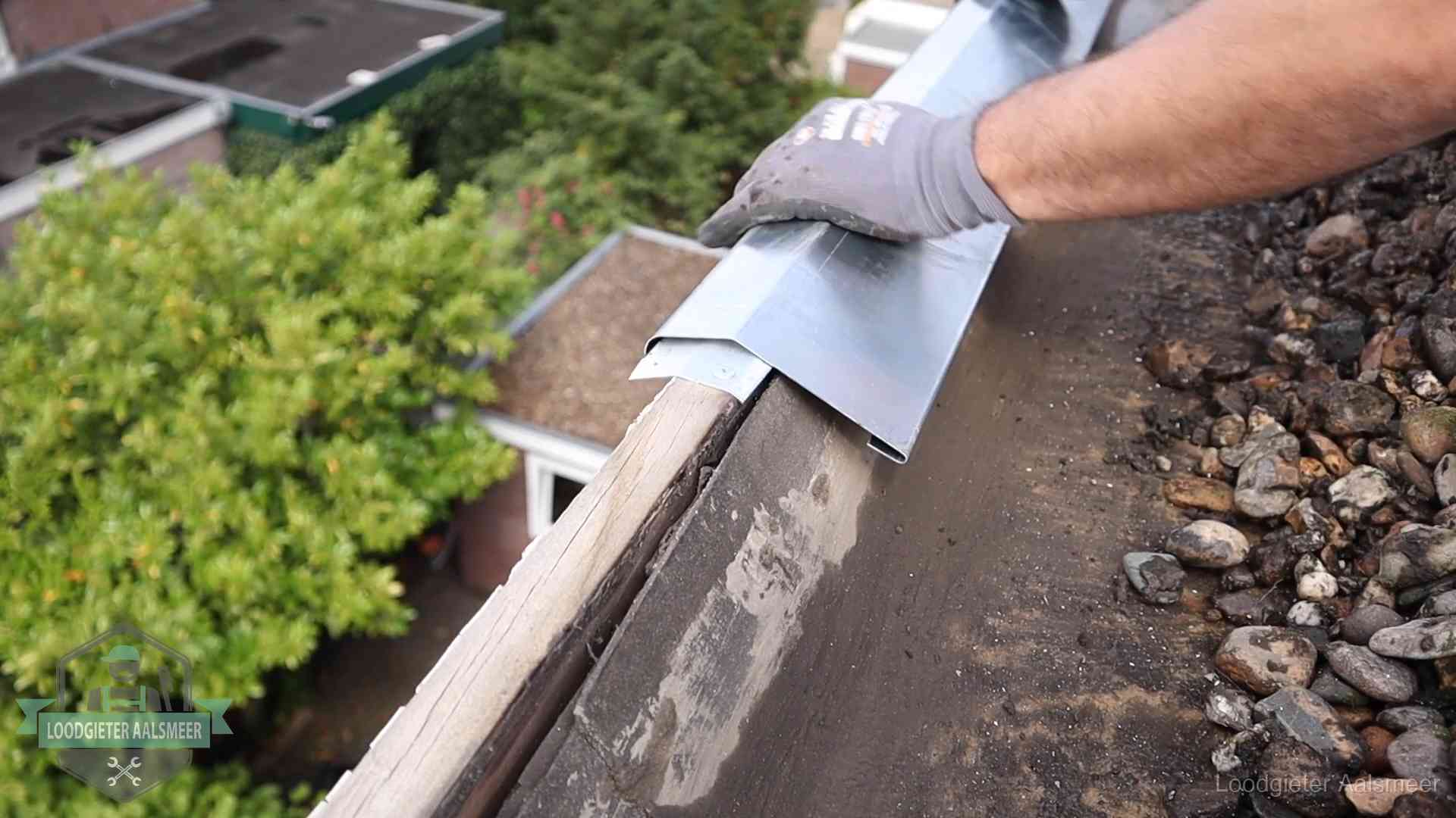 Dakdekker plaatst een zinken deklijst op een dakrand met uitzicht over een woonwijk in Aalsmeer
