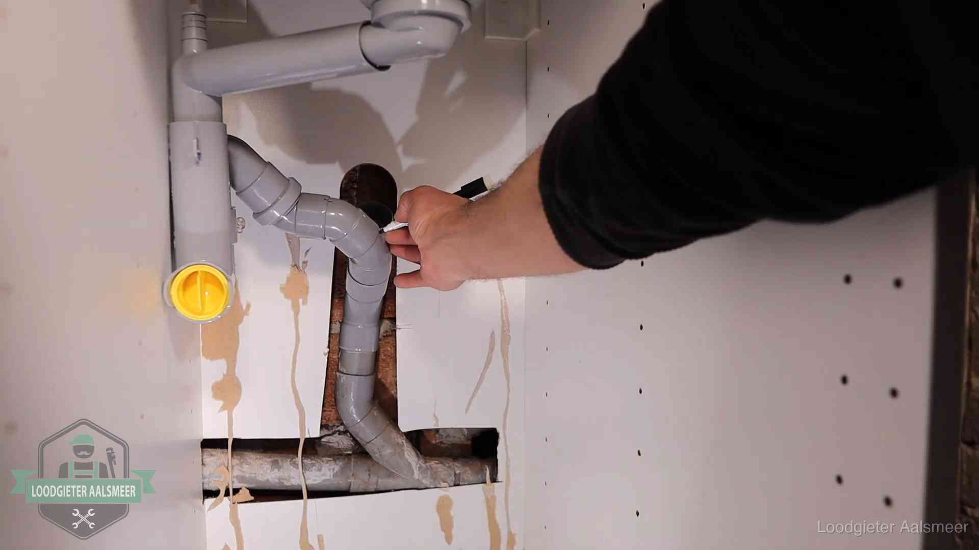 Loodgieter markeert een pvc-afvoerbuis onder een gootsteen in Aalsmeer