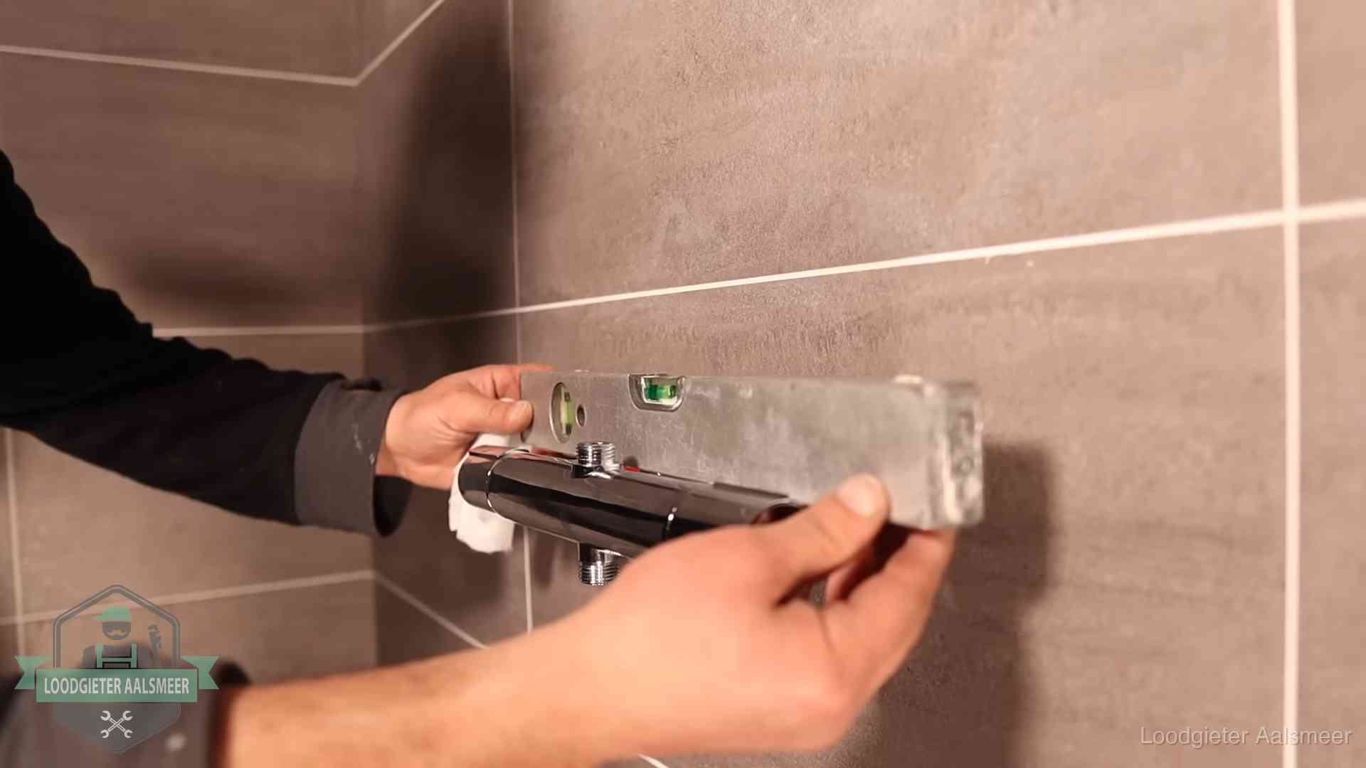 Loodgieter lijnt een douchekraan uit met een waterpas in een woning in Aalsmeer