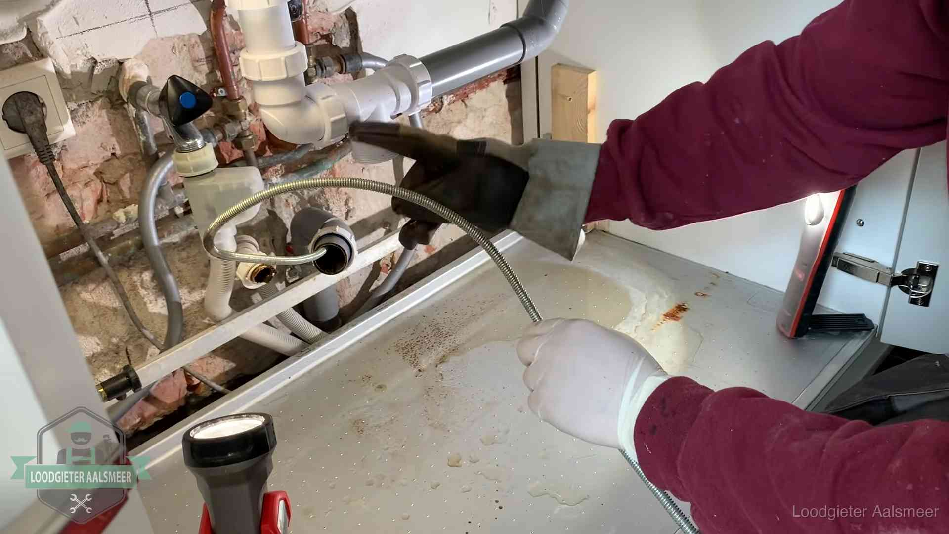 Ontstoppingsveer gaat in een geopende sifonaansluiting onder het aanrecht in Aalsmeer