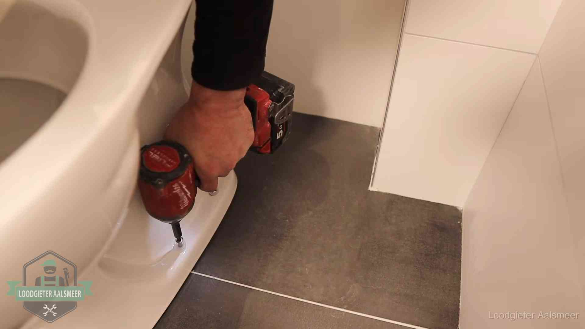 Loodgieter zet de voet van een wc-pot vast op de tegelvloer in Aalsmeer